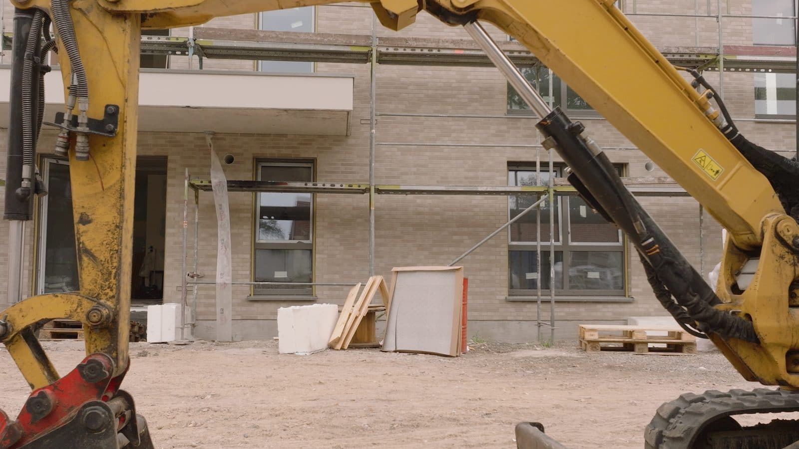 Baggerarm vor der Klinkerfassade eines Neubaus mit Gerüst